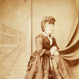 Studio portrait of a woman standing in front of a painted backdrop. Sandhurst (Bendigo), Victoria, circa 1872.